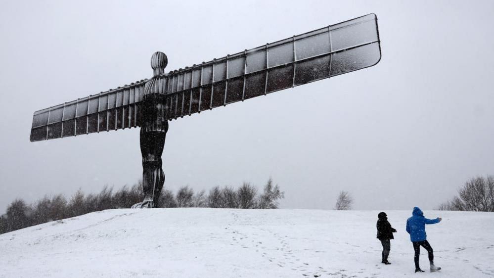 People walk next to Antony Gormley's Angel of the North as snow continues to fall in Gateshead