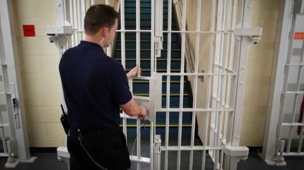 Prison guard locking a door with bars inside Cookham Wood Young Offenders Institution, Rochester