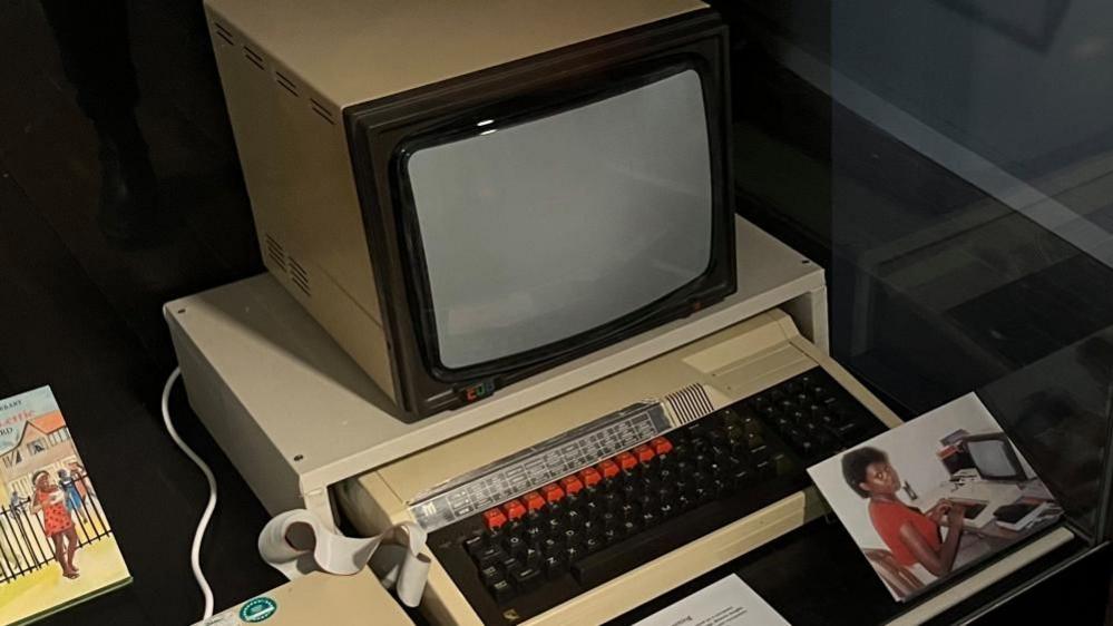 The BBC Computer, which Malorie Blackman used inside an exhibition display case, with a picture of her using it.