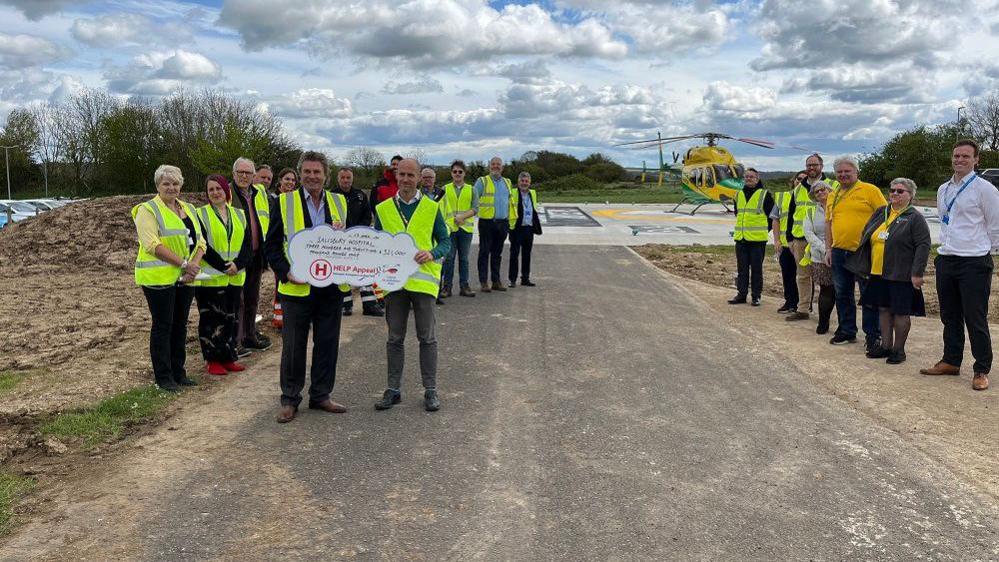 Two rows of people in high-vis in front of the helipad looking at the camera