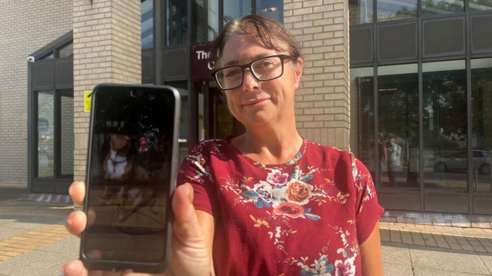 Emily Moore standing outside court holding her mobile phone showing a picture of her dog Havana