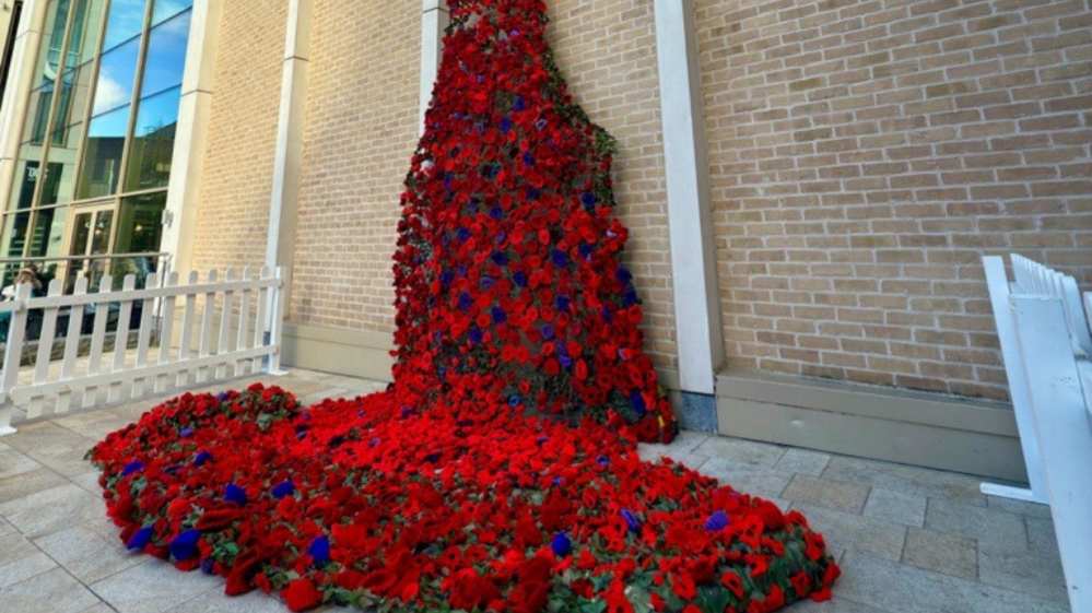 Lots of red and purple flowers are grouped together to form a flowing display that falls down the side of the building and pools on the ground.