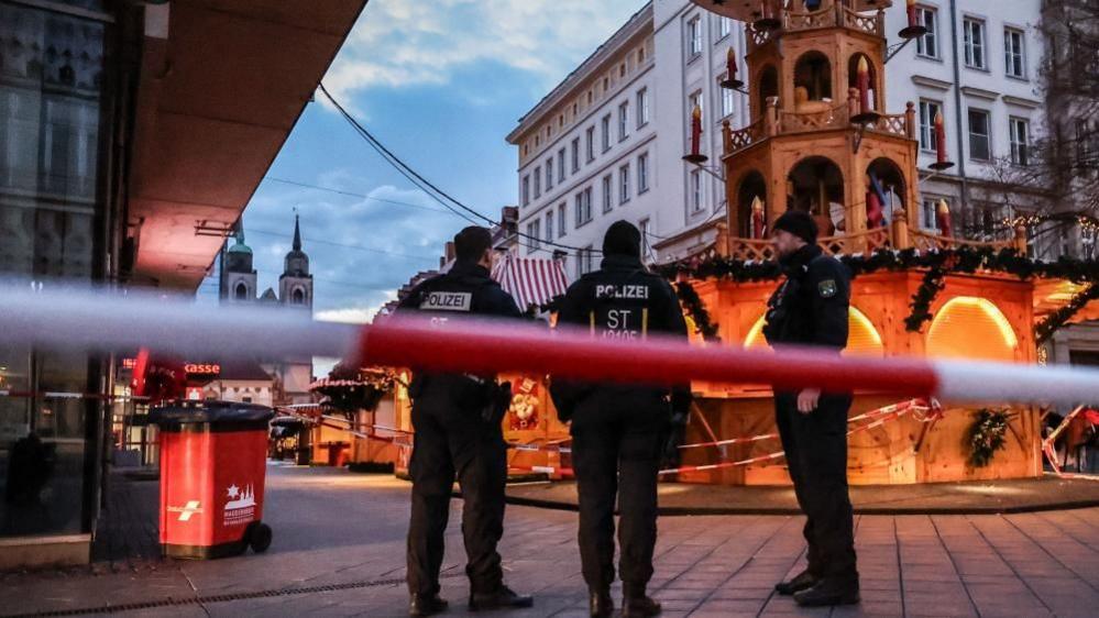 Three German police officer stand behind red and white police tape by the Christmas markets