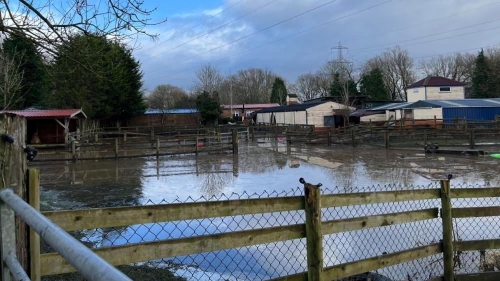 A field completely full of deep floodwaters. The tops of fences can be seen poking up through the water