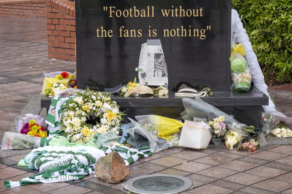 Flowers, a football strip and newspaper clippings left at the foot of a black marble statue which reads "Football without fans is nothing"