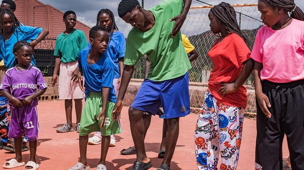 Members of the Ugandan dance group the Ghetto Kids rehearse at their home in Nakawuka, Uganda, on 25 May 2026. They are wearing an array of brightly coloured T-shirts and mimicking the moves of an adult man choreographer. 