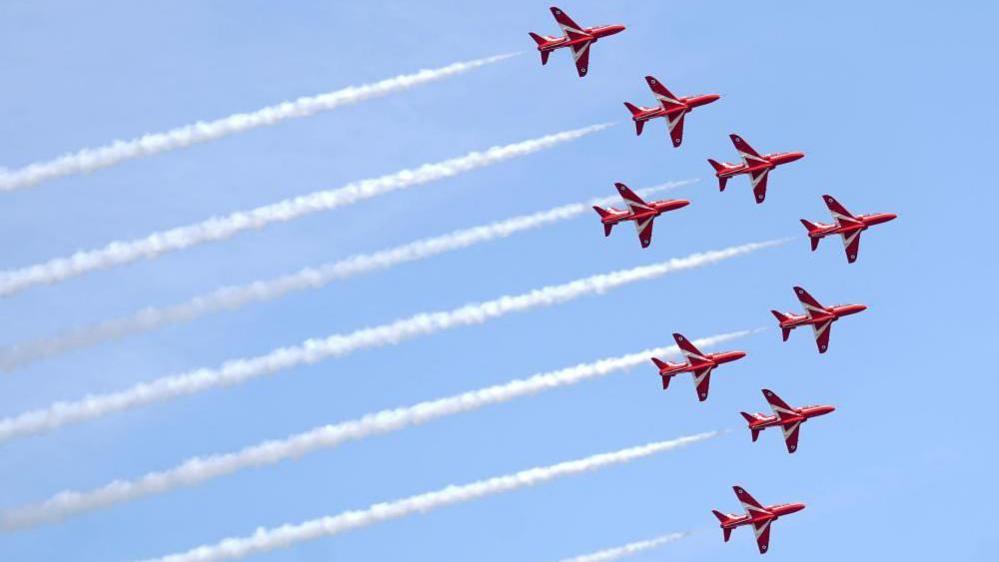 The Red Arrows fly in formation with a white vapour trail 