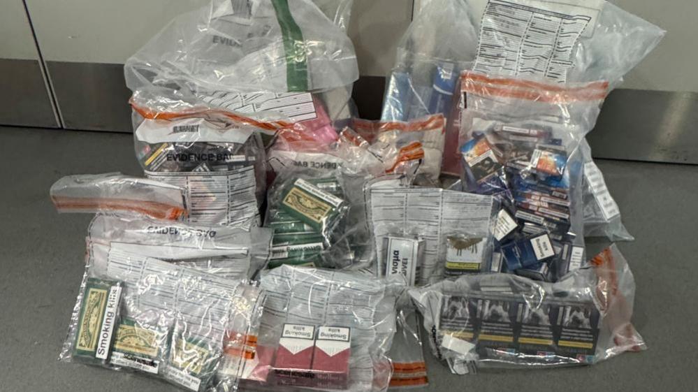 Eight plastic bags of illegal tobacco are pictured in a rom which has grey walls and grey floors. 