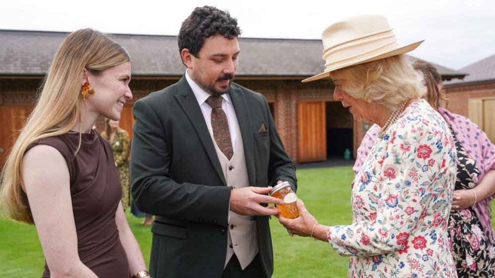 Queen Camilla is presented with a jar of honey by Harry and Seline Silk from Knavesmire Nectar.