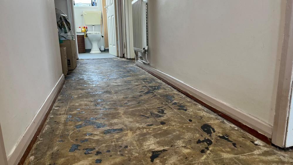 Concrete floor with remnants of vinyl glue where his laminate floor had been taken up owing to sewage leaking into the area