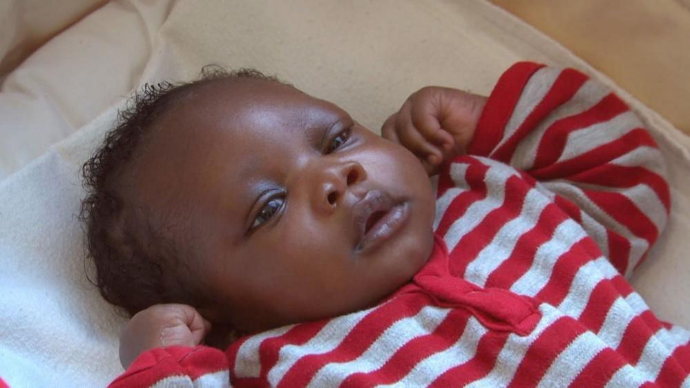 A photo of baby laying on his back looking upward. He is wearing a red and white striped body suit