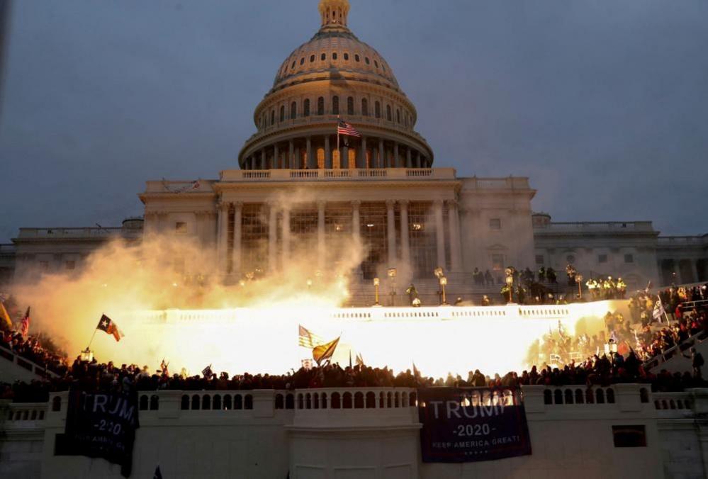 An explosion caused by a police munition lights up the front of the US Capitol building in Washington on 6 January 2021. Trump supporters are gathered there.