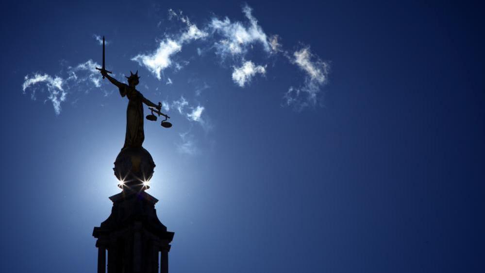A state of Lady Justice on top of the Old Bailey / Central Criminal Court, with a blue sky in the background.