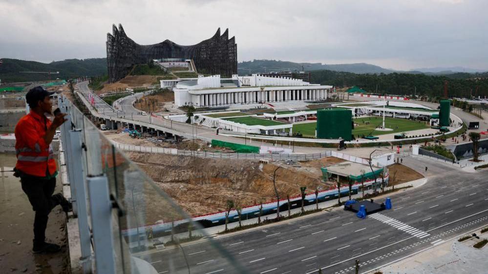 A construction worker stands on a platform looking out at the future Presidential Palace