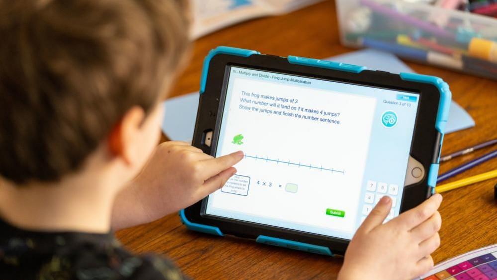 Stock image of a young boy looking at a maths problem on an iPad.