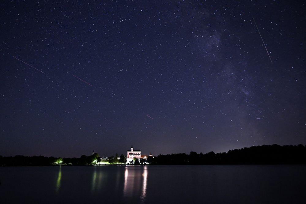 A meteor streaks as satellites cross the night sky over a monastery