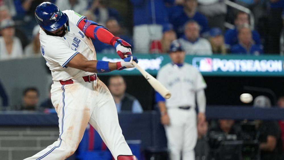 Vladimir Guerrero Jr swings at a pitch. He's wearing a white Blue Jays uniform with blue trim.
