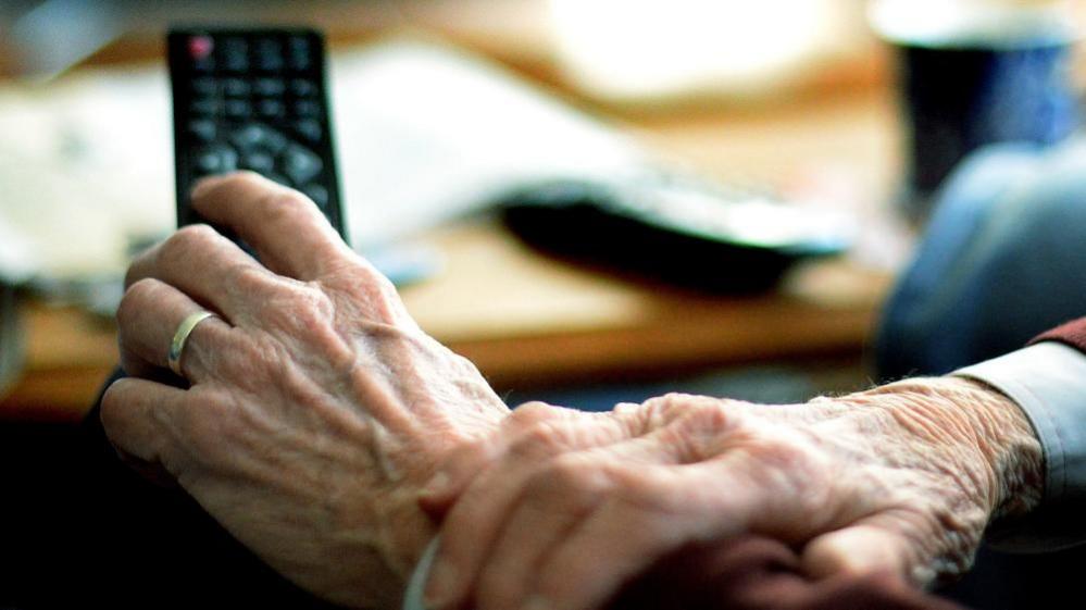 A closeup picture of a hand holding a remote control with their other hand holding their wrist