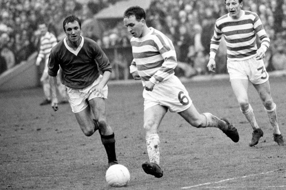 A black and white photo of three footballers, two in stripped celtic tops, the man in the middle has a number six on his shorts and kicks a whie ball