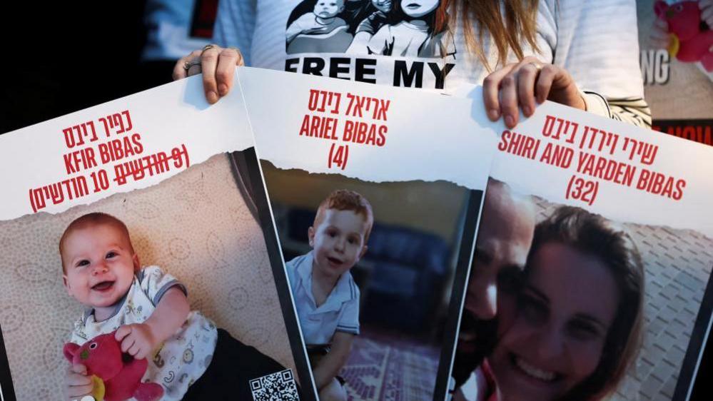 A protester holds signs calling for the release of hostages of Shiri Bibas and her children Kfir and Ariel