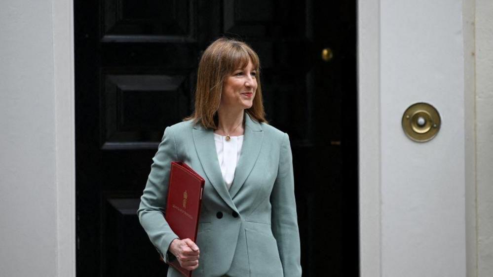 Chancellor Rachel Reeves smiles as she leaves No 11 Downing Street holding a red folder. 