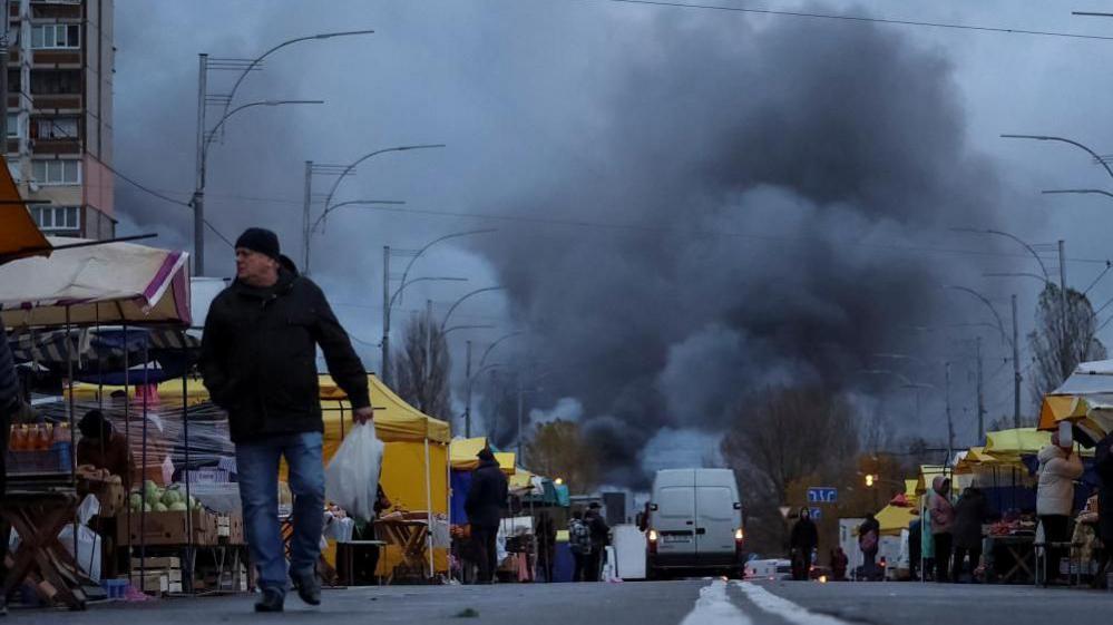 A man walks around a market as a fire burns at the site of a missile strike