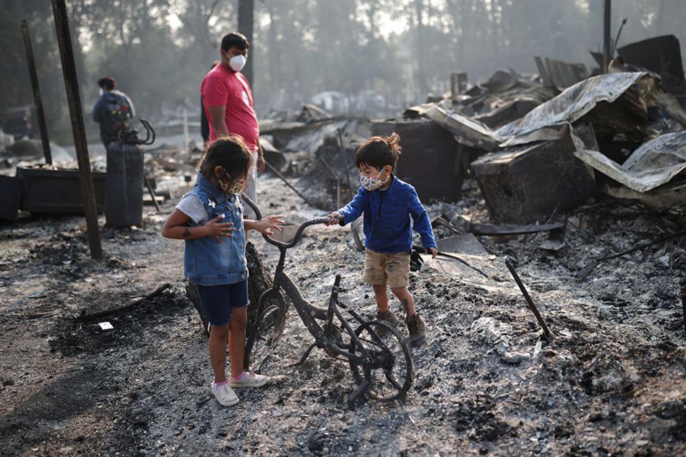 Ashley, 3, and Ethan, 2, look at a burned bicycle after wildfires destroyed a neighbourhood in Bear Creek, Phoenix, Oregon