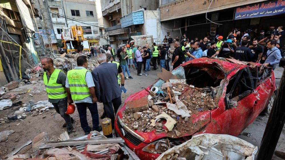 People stand next to a destroyed car, at the site of an Israeli strike in Beirut's southern suburbs, Lebanon September 24, 2024.