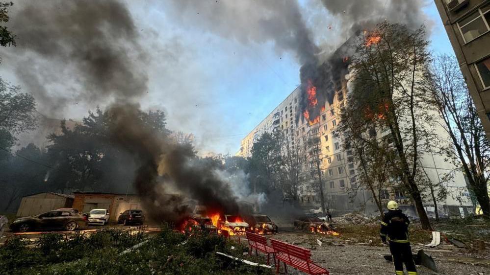 A firefighter looks at an apartment building and cars which burn after a Russian air strike in Kharkiv, north-eastern Ukraine