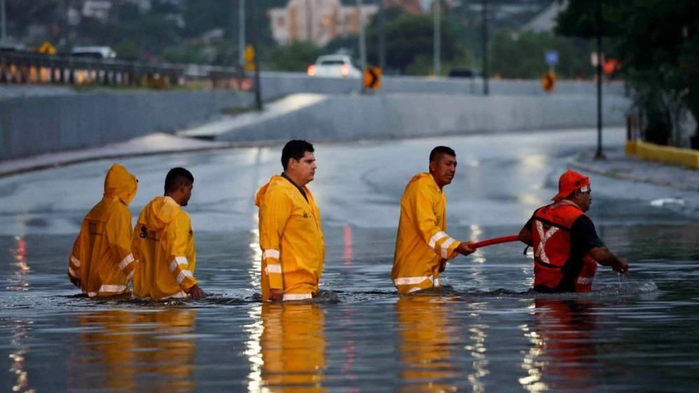 Five workers wade through a flooded road