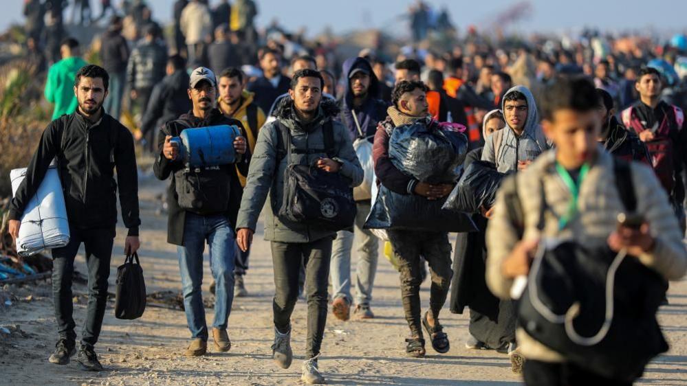 The image shows several Palestinian men carrying their belongings arriving on foot as they make their way back to their homes in northern Gaza.  