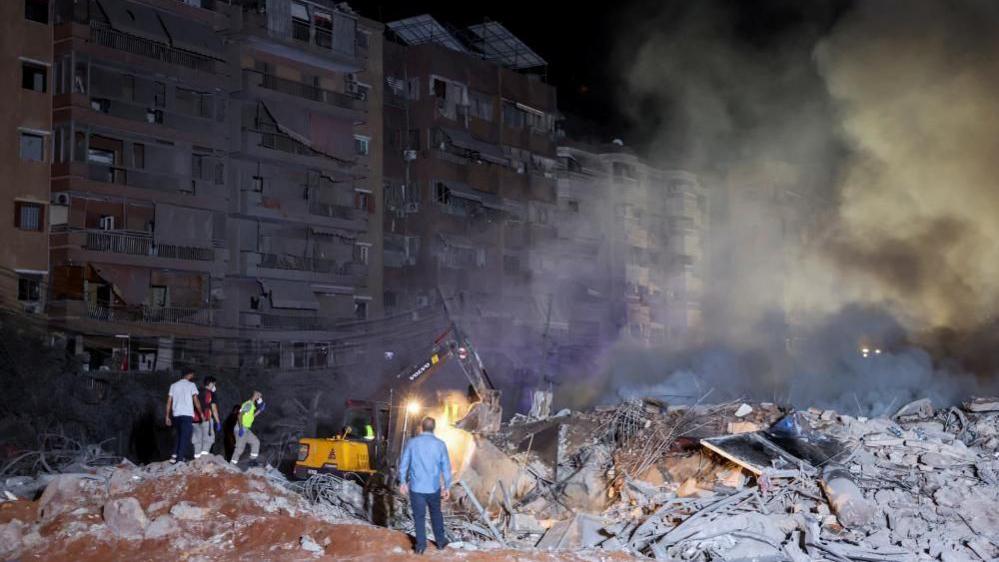 People inspect damage at the site of an Israeli strike in Dahiyeh