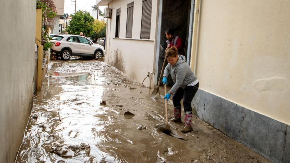 A woman cleans mud off a street following floods caused by storm Bora in the area of Lalysos, on the island of Rhodes, Greece, 1 December 2024