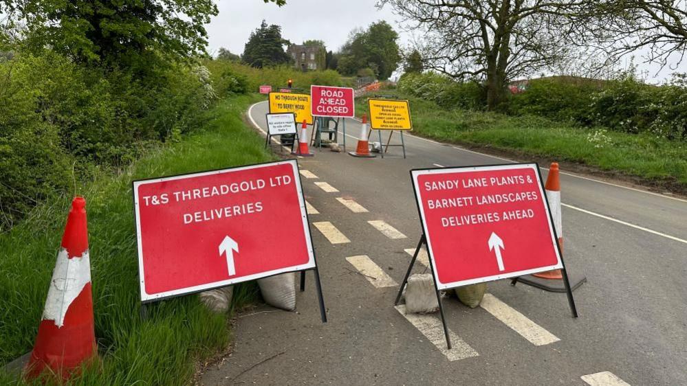 Road closure in rural area with red signs showing access for deliveries