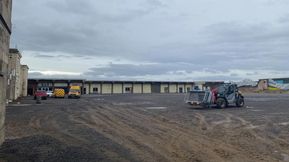 Construction vehicles drive around the back of the Tropicana building.