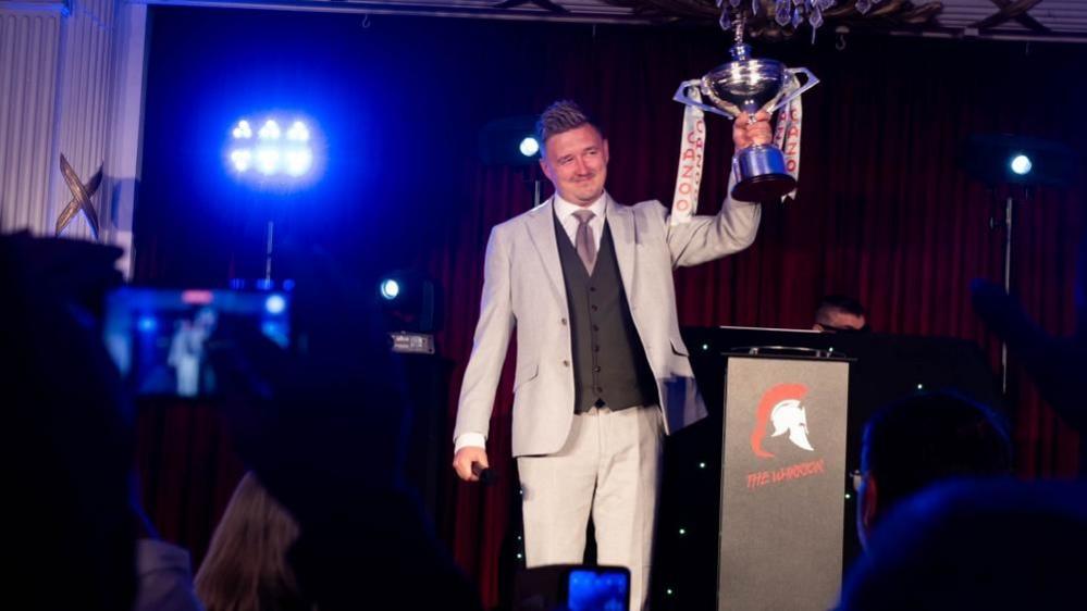 Wilson holding up trophy with left hand