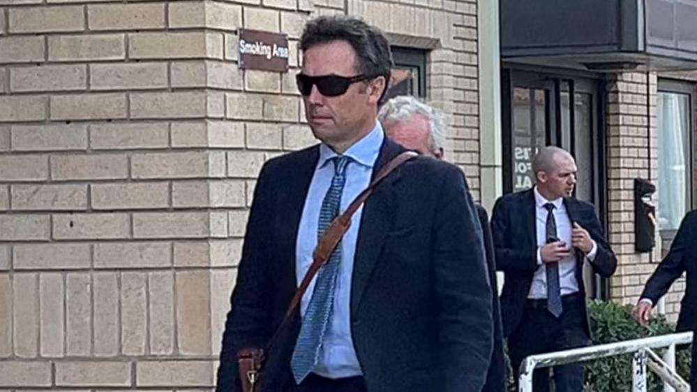 Robert Gurney, wearing a suit and sunglasses on his way into court