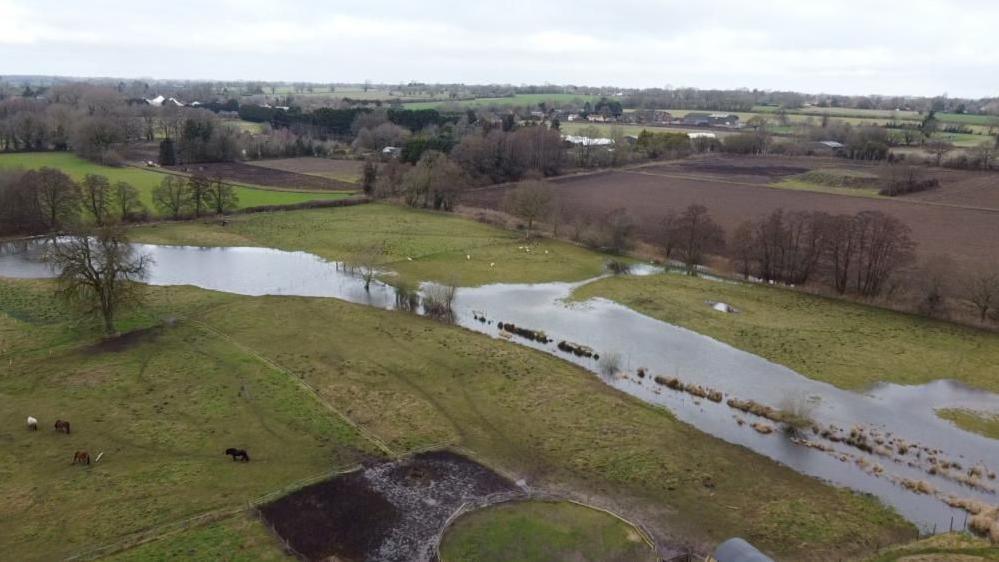 A picture of landscape from up high. there are fields in the back ground. In the foreground the you can see an area is flooded which is following the old river channel. 