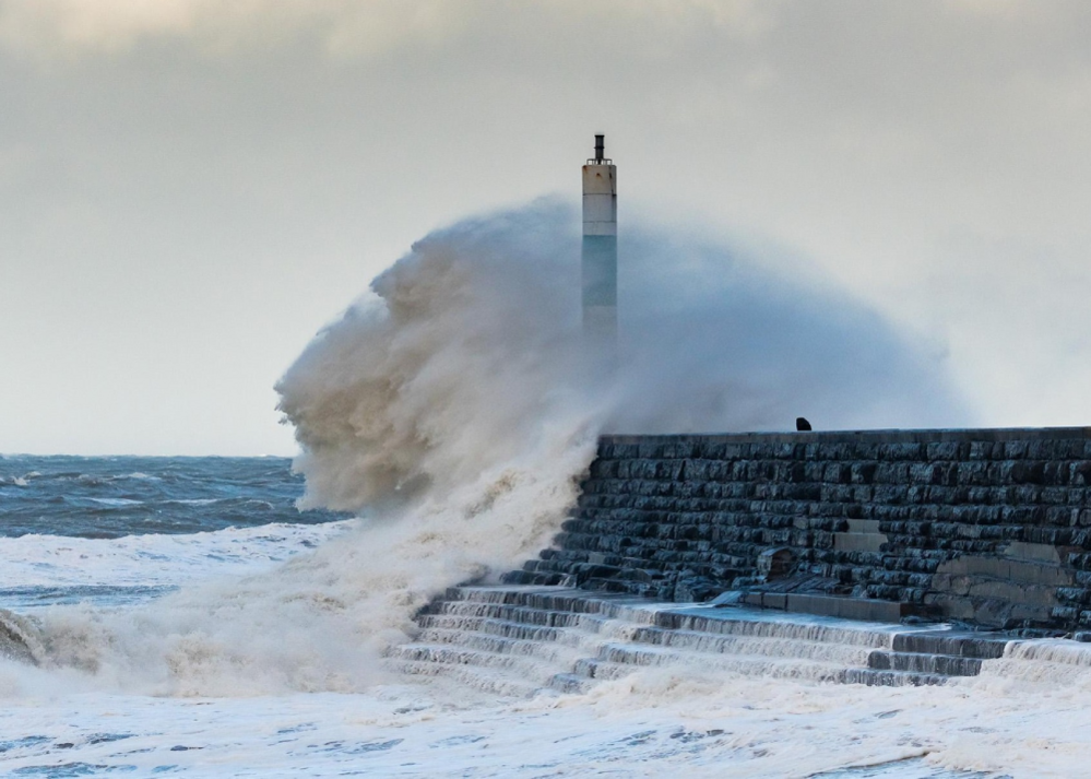 Waves crash over the navigation light at the end of the jetty at the entrance to Aberystwyth harbour