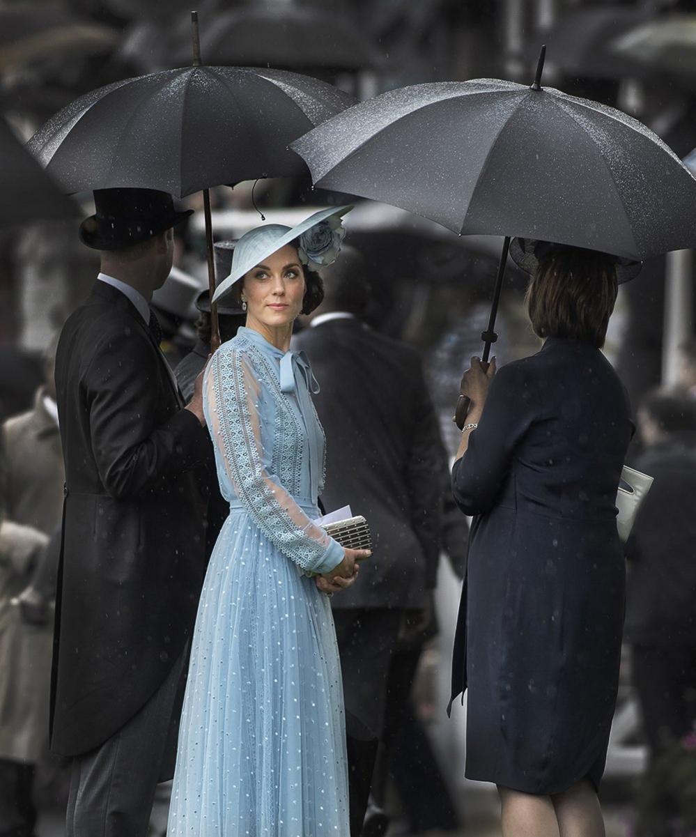 The Duchess Of Cambridge shelters under Prince William's umbrella