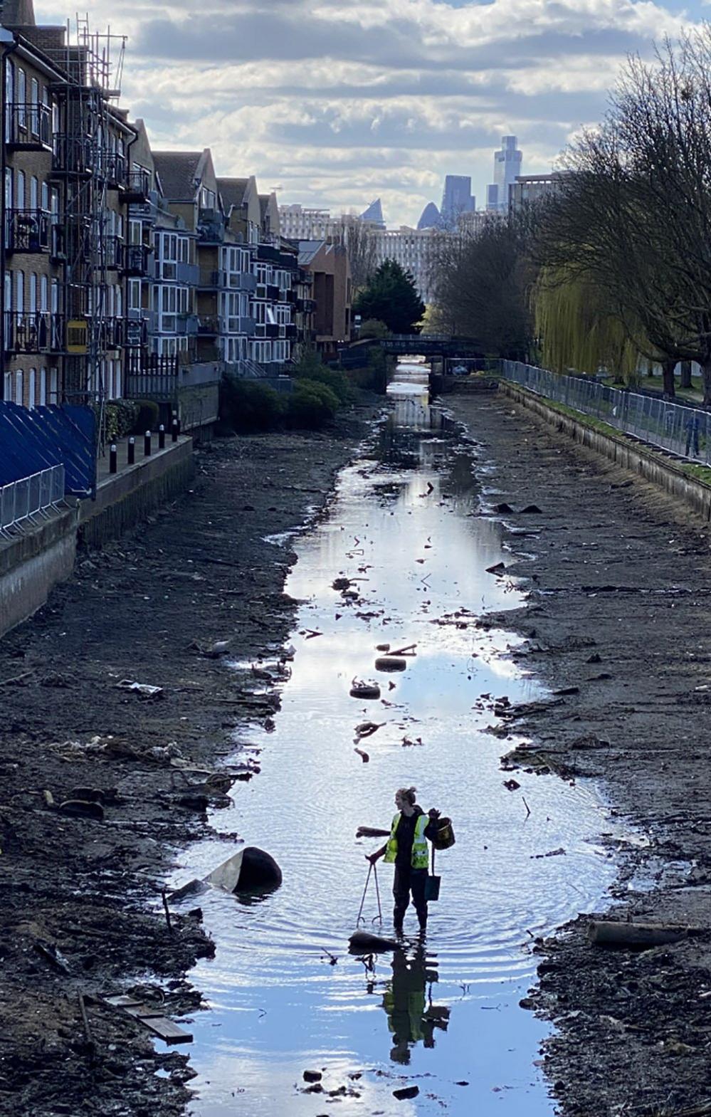 A volunteer litter-picker removes rubbish from the drained Hertford Union Canal