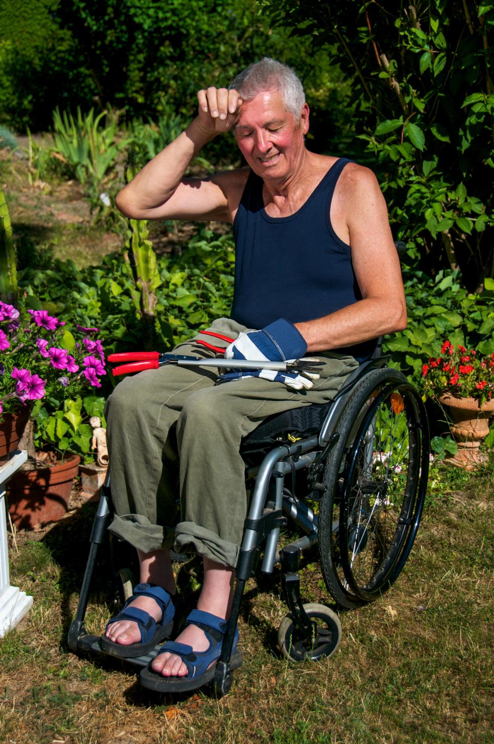 Man in wheelchair sweltering in a sunny garden