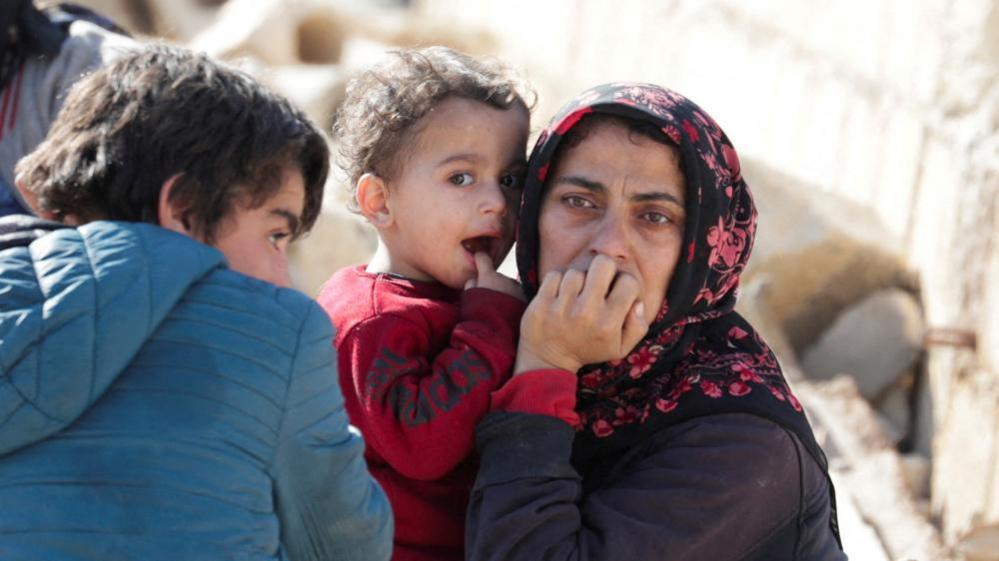 A woman holds a child amid rubble