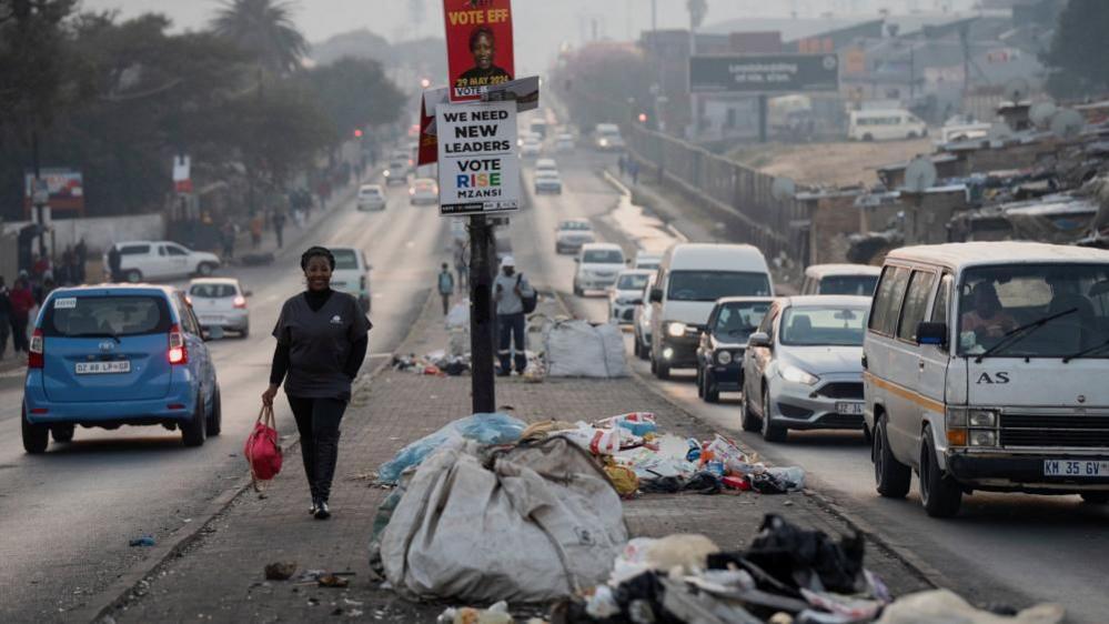 A woman walks past piles of uncollected trash in the township of Alexandra a day before the national election in Johannesburg, South Africa May 28, 2024