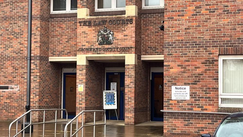 Norwich Crown Court is a red brick building, built in the 1980s. It has a Royal Crest above the door and the text "The Law Courts" above, and "Crown and County Court" beneath. There are three entrances, and windows featured in the brickwork, with steps and chrome railings on the approach.