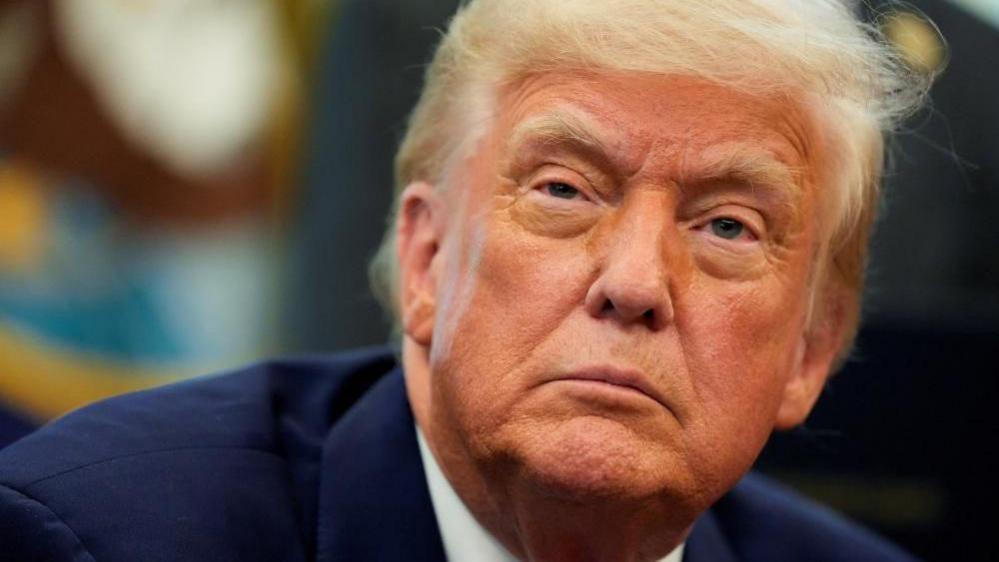 A close-up of President Donald Trump's face, bearing a serious expression