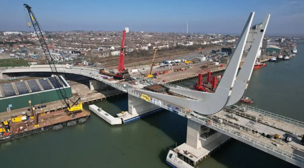 A drone image of the Gull Wing Bridge during construction showing large J beams at one end and two cranes