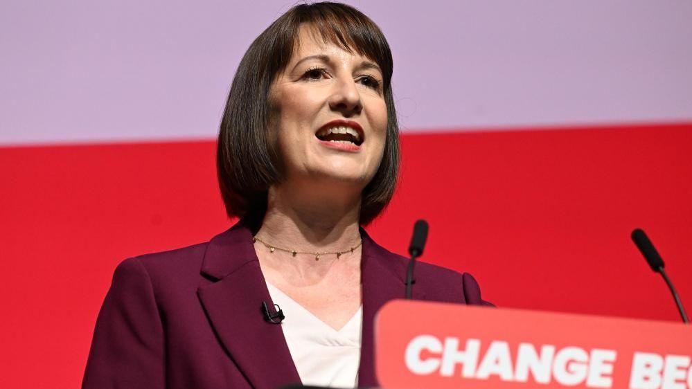 Rachel Reeves speaks into a microphone in front of a red background