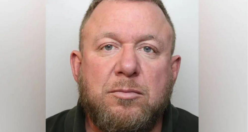 A police custody head and shoulders mugshot of Mark Killick. He is looking straight at the camera and is wearing a dark shirt with a collar. He has short cropped ginger hair, and a mid-length beard and moustache.