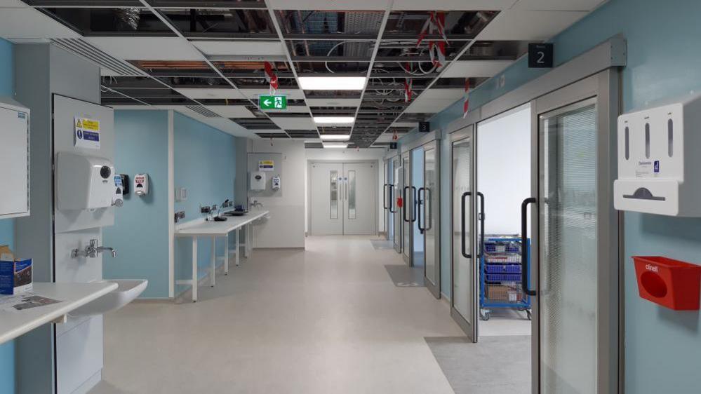 A corridor in the new urgent and emergency care centre, with sinks along one wall and rooms with open doors opposite.